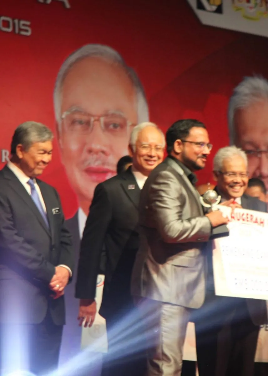 Trishank receiving an award on stage at a 2015 national awards ceremony, with Malaysia's then Prime Minister and then Deputy Prime Minister present